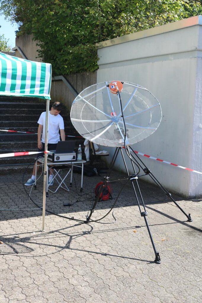 Ein Stativ mit einer großen, runden Antenne steht neben einem Tisch und einer Person.