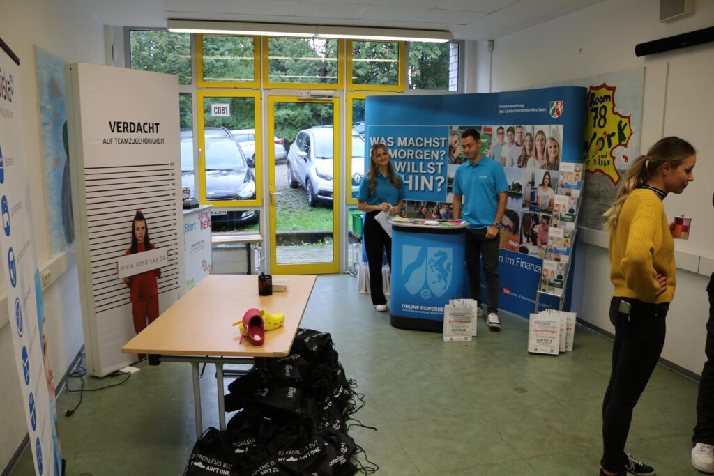 Messestand mit zwei Personen, Informationsmaterial und einem Tisch in einem Raum.