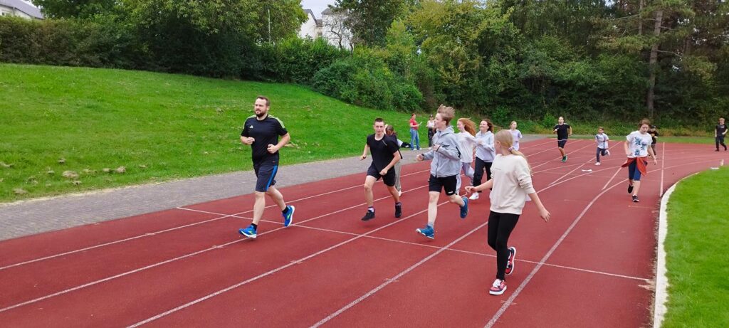 Gruppe von Schülern und Lehrern beim Laufen auf einer Laufbahn.