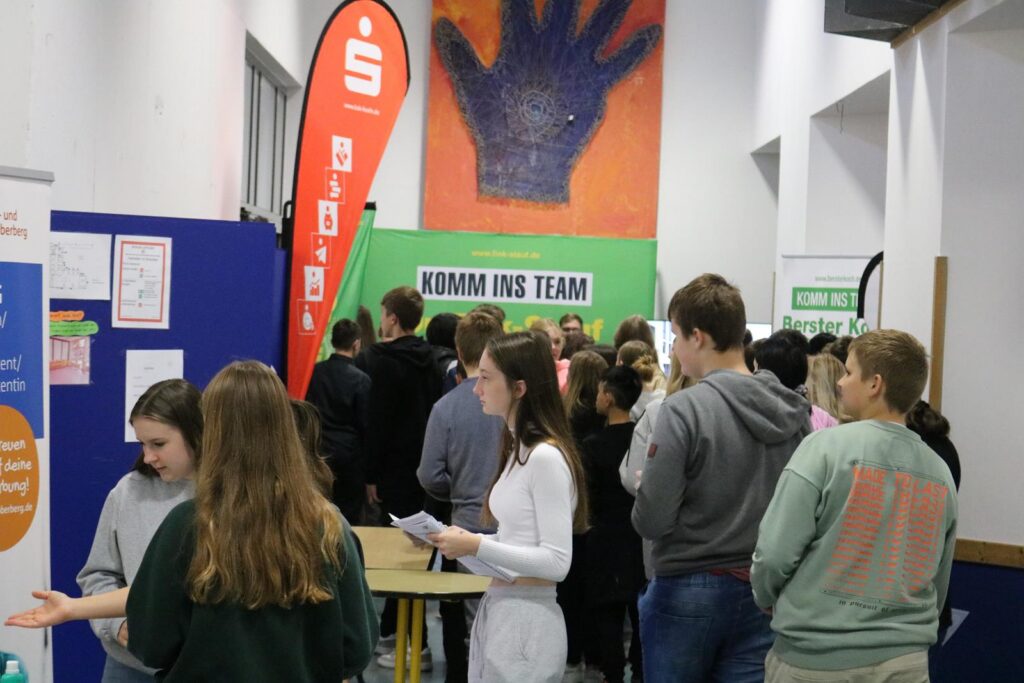 Schüler stehen an Informationsständen in einem Schulgebäude.