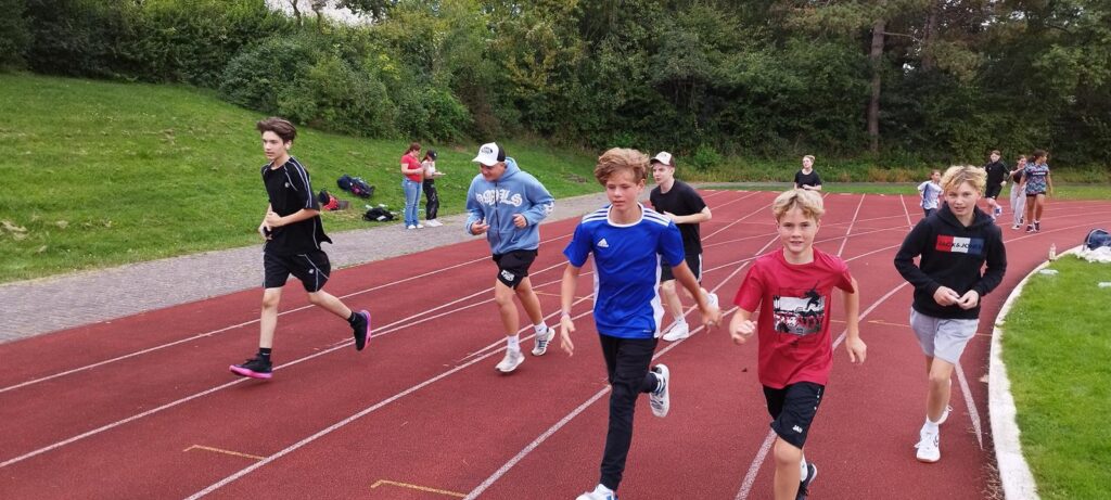Schülerinnen und Schüler laufen auf einer Tartanbahn.