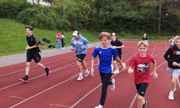 Schülerinnen und Schüler laufen auf einer Tartanbahn.
