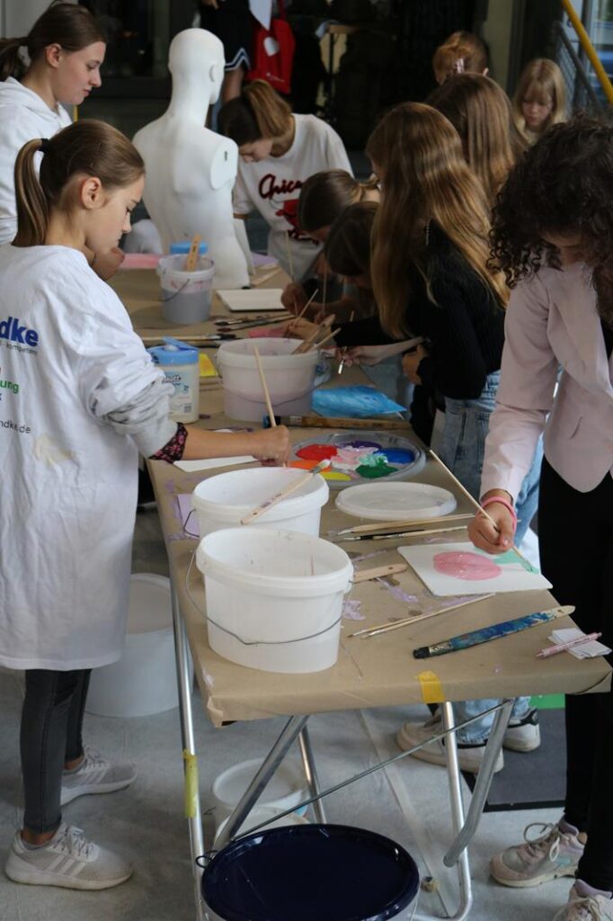 Schülerinnen und Schüler malen an Tischen mit verschiedenen Farben und Materialien.