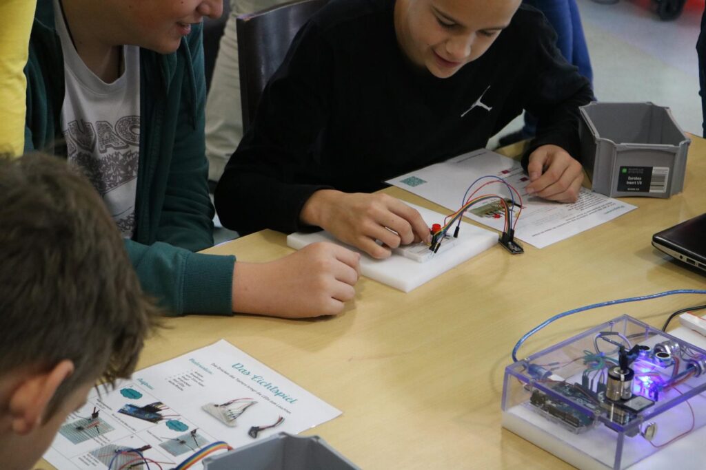 Schüler arbeiten mit elektronischen Bauteilen und Anleitungen am Tisch.