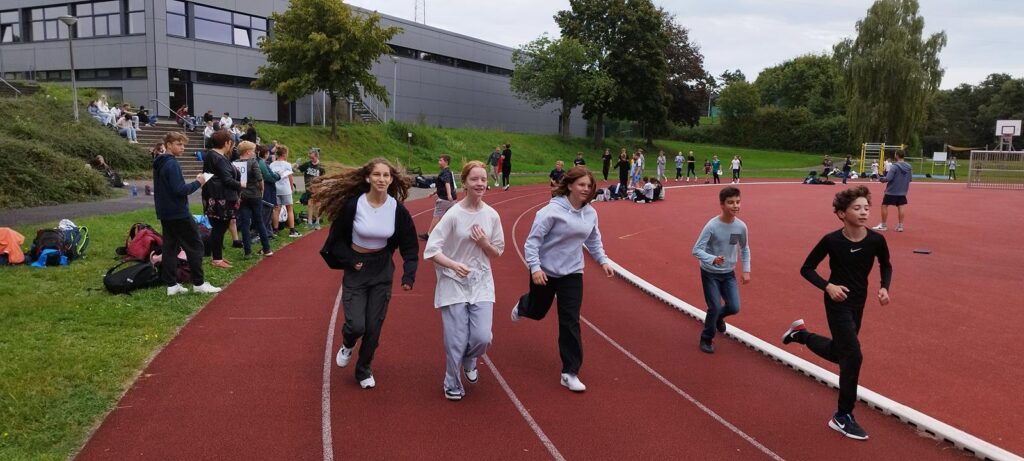 Schüler laufen auf der Laufbahn, Zuschauer sitzen auf den Rängen.