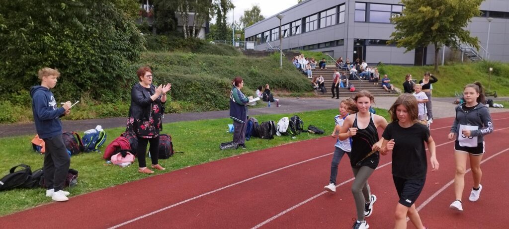 Schüler laufen auf der Laufbahn, Zuschauer applaudieren im Hintergrund.