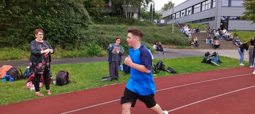 Schüler läuft auf der Laufbahn, Zuschauer im Hintergrund.