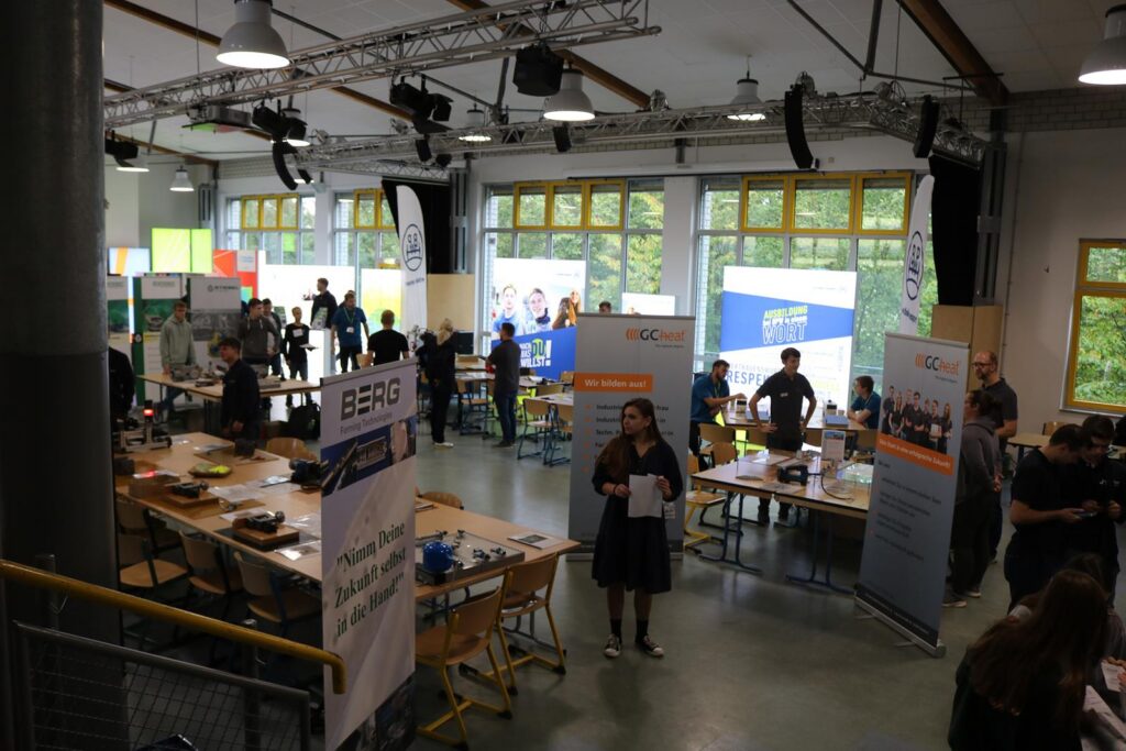 Veranstaltung in einer Halle mit Ständen, Tischen und Menschen im Austausch.