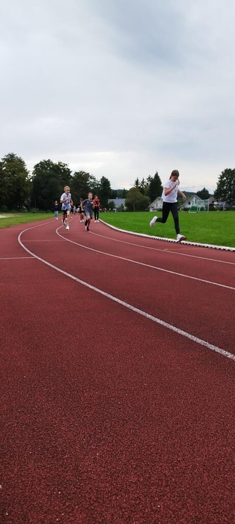 Schüler laufen auf einer roten Laufbahn in einem Sportfeld.
