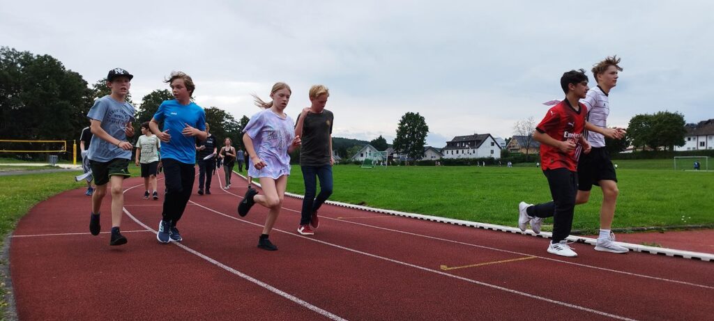Schüler laufen auf einer Rennbahn, umgeben von Grünflächen und Bäumen.