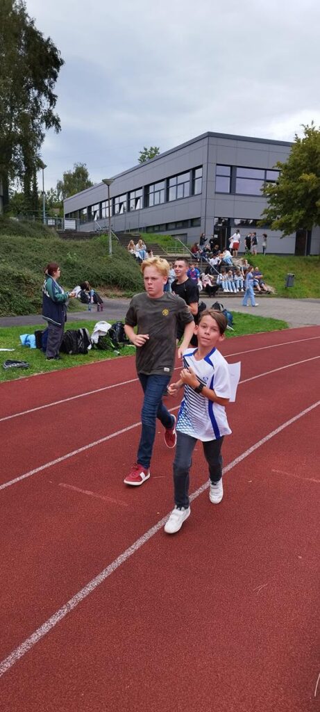 Schüler laufen auf der Laufbahn, Zuschauer im Hintergrund.