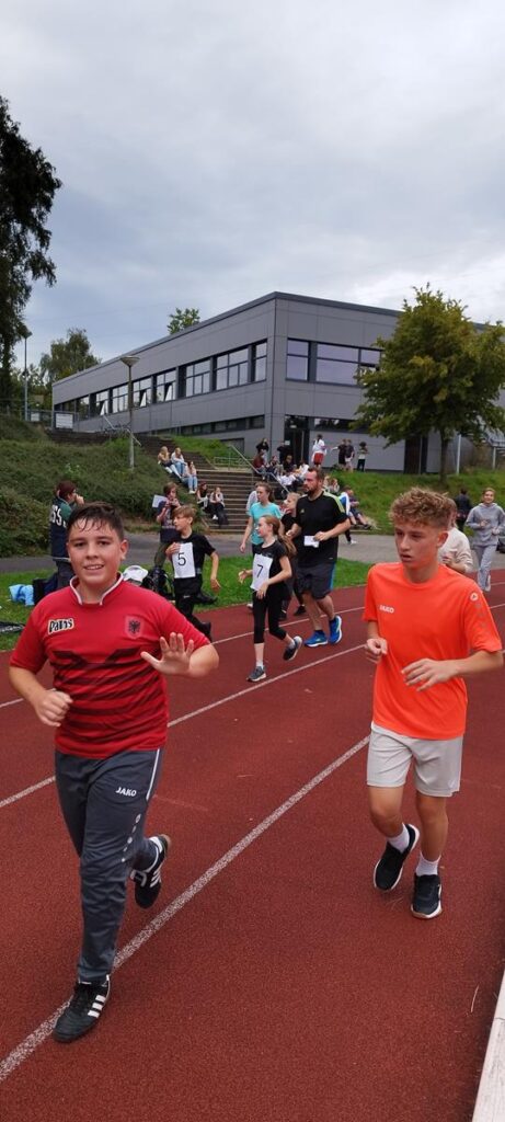 Kinder laufen auf einer Laufbahn, Zuschauer im Hintergrund, Sportveranstaltung.