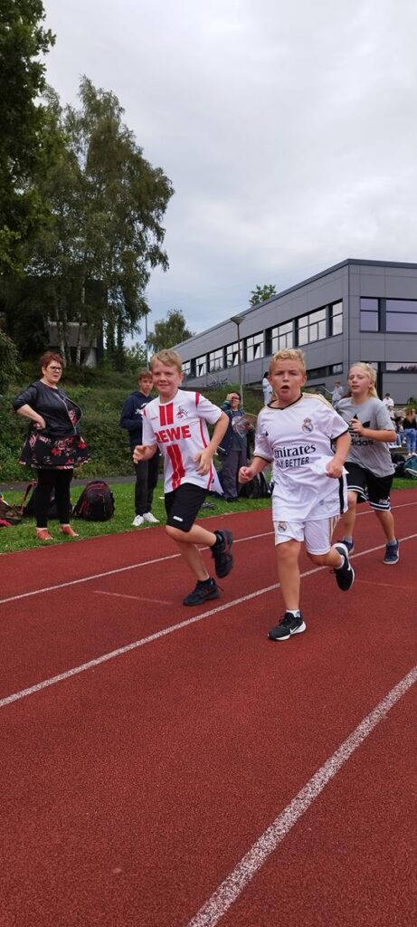 Schülerinnen und Schüler laufen auf einer Laufbahn während eines Sportereignisses.