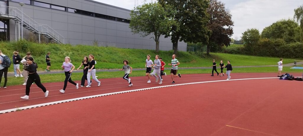 Schülerinnen und Schüler laufen auf einer Laufbahn im Freien.