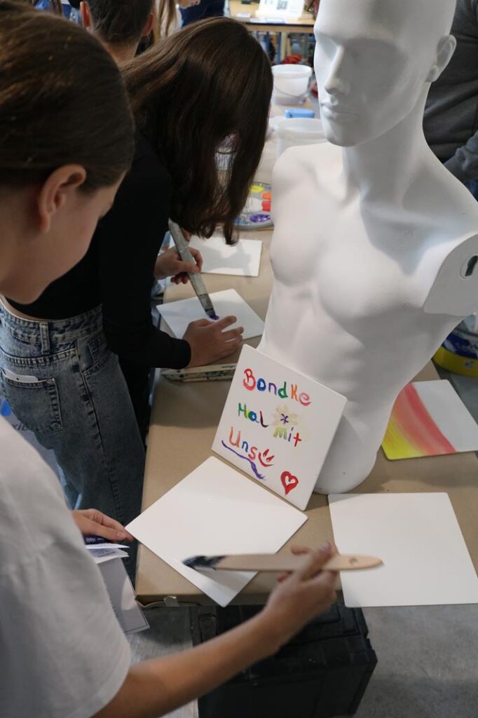 Schüler bemalen Papier und gestalten Kunstwerke an einem Tisch.