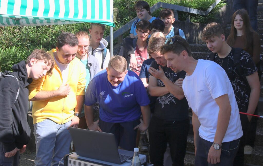 Gruppe von Schülern versammelt sich um einen Laptop im Freien.