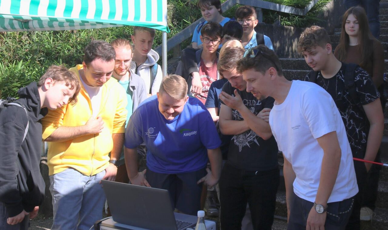 Gruppe von Schülern versammelt sich um einen Laptop im Freien.