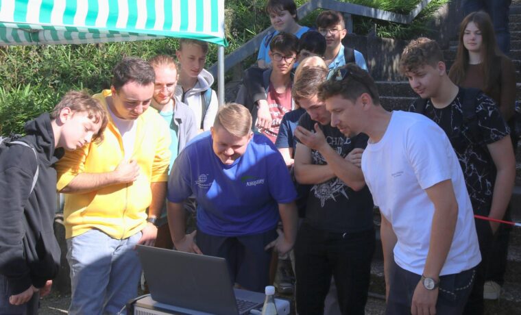 Gruppe von Schülern versammelt sich um einen Laptop im Freien.