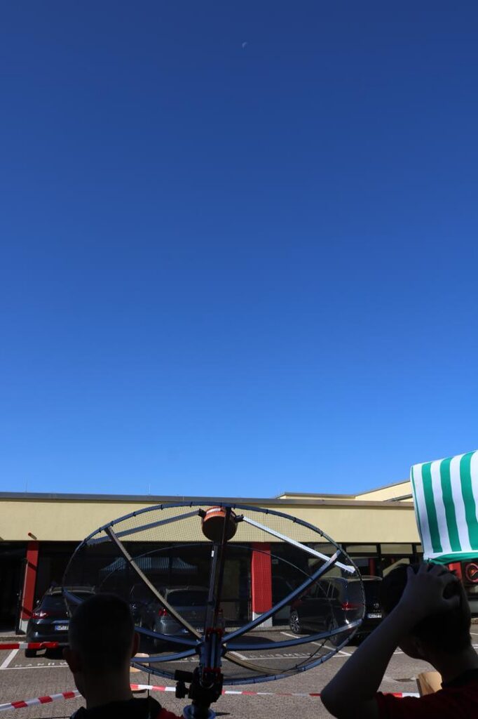 Personen beobachten mit einem Gerät den Himmel unter klarem blauen Himmel.