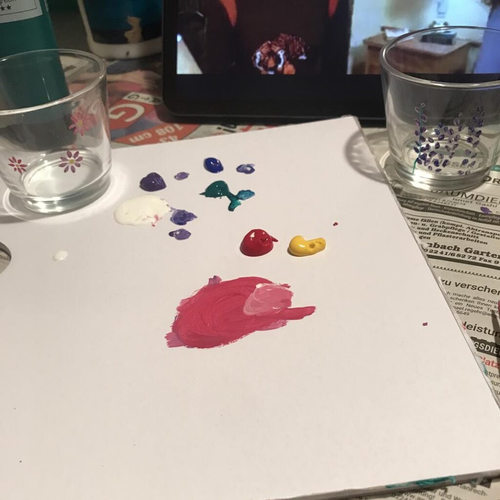 Farben auf einem Blatt Papier und zwei Gläser mit Farben im Hintergrund.