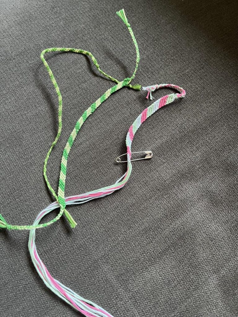 Bunte Freundschaftsbänder und eine Sicherheitsnadel auf grauem Hintergrund.