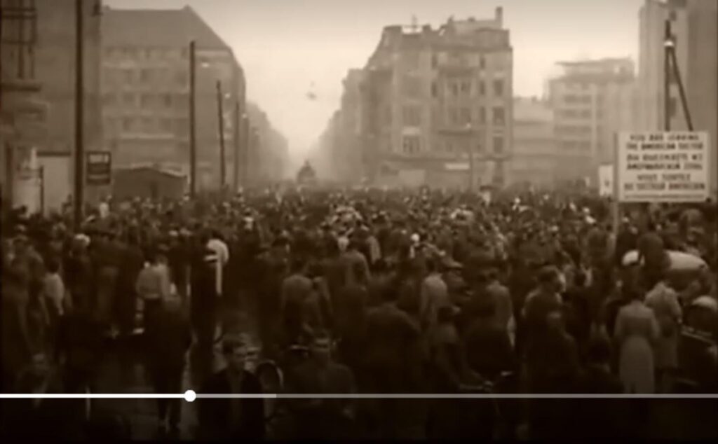Menschenmenge auf einer Straße, umgeben von historischen Gebäuden.