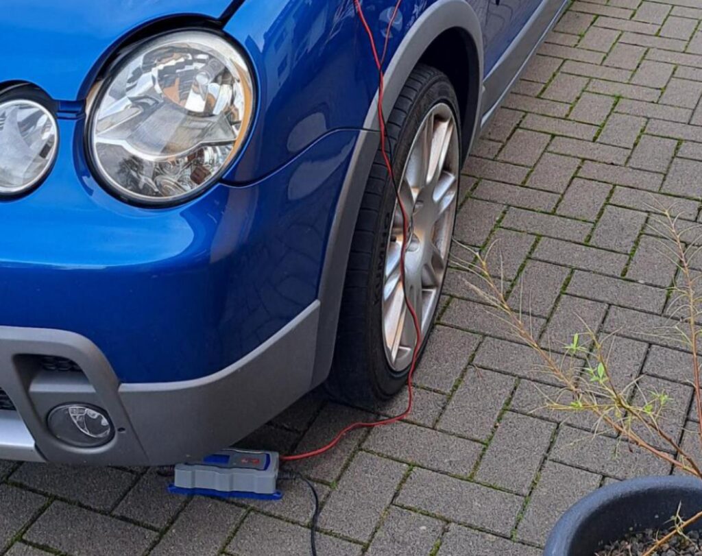 Blauer Wagen mit verbundenem Ladegerät und plattgedrücktem Reifen.