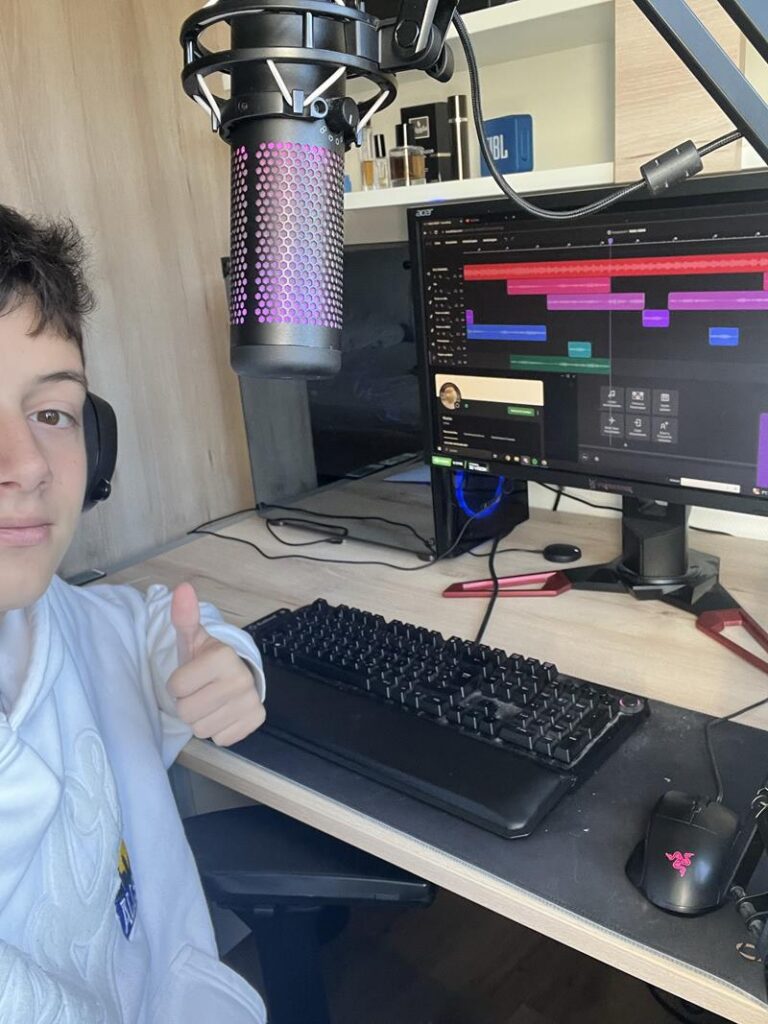 Junge zeigt Daumenhoch vor einem Computer mit Mikrofon und Monitor.
