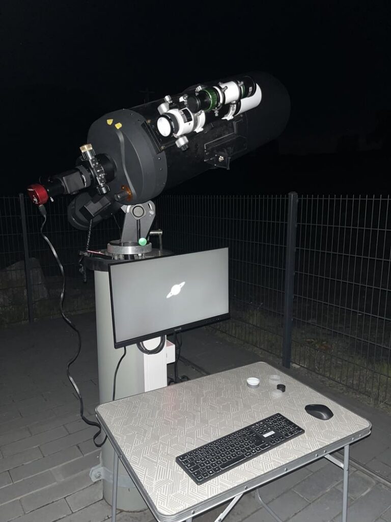 Teleskop auf einem Stativ mit einem Computer und Zubehör bei Nacht.