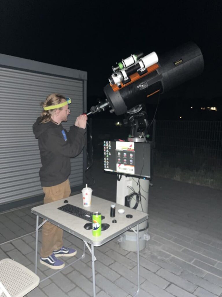 Eine Person beobachtet durch ein Teleskop auf einer Außenterrasse bei Nacht.