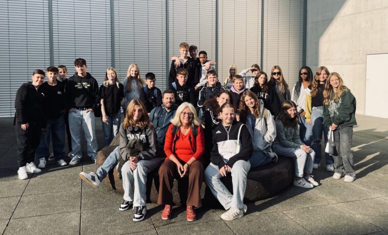 Gruppe von Schülern und Lehrern posiert gemeinsam auf einer Sitzgelegenheit im Freien.