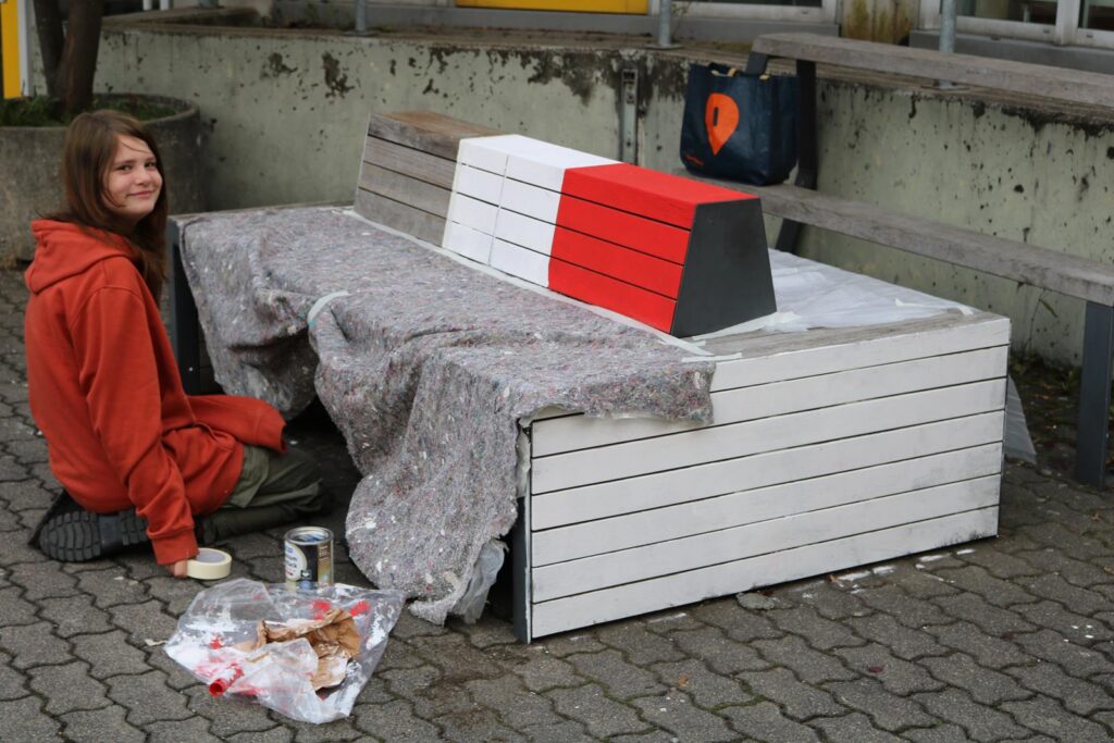 Ein Mädchen sitzt auf dem Boden neben einer lackierten Bank.