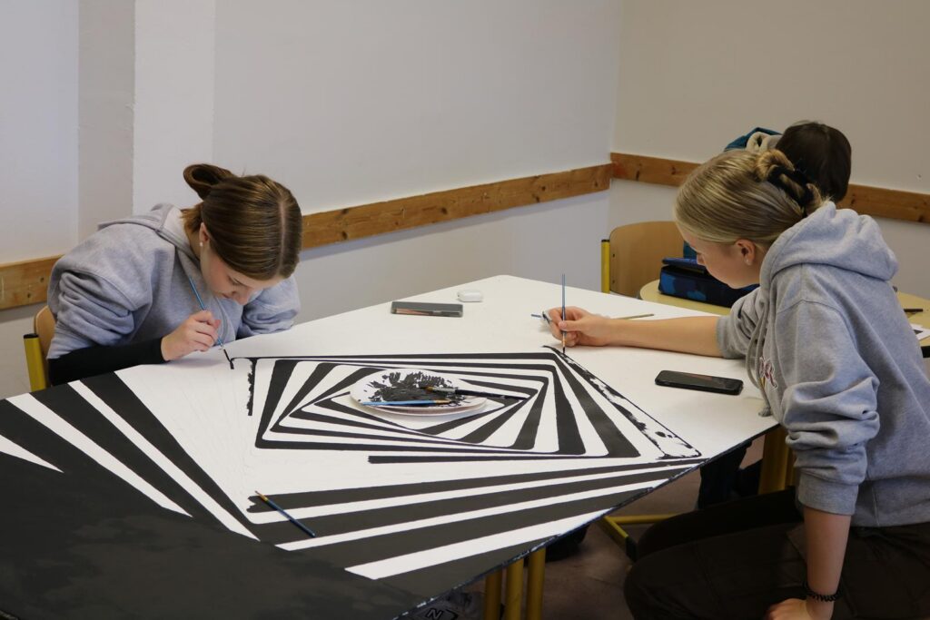 Schülerinnen malen an einem großen Schwarz-Weiß-Gemälde im Kunstraum.