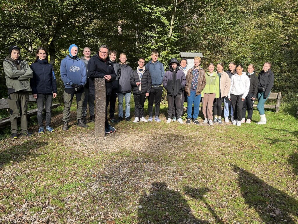 Gruppe von Schülern steht im Freien auf einer Wiese umgeben von Bäumen.