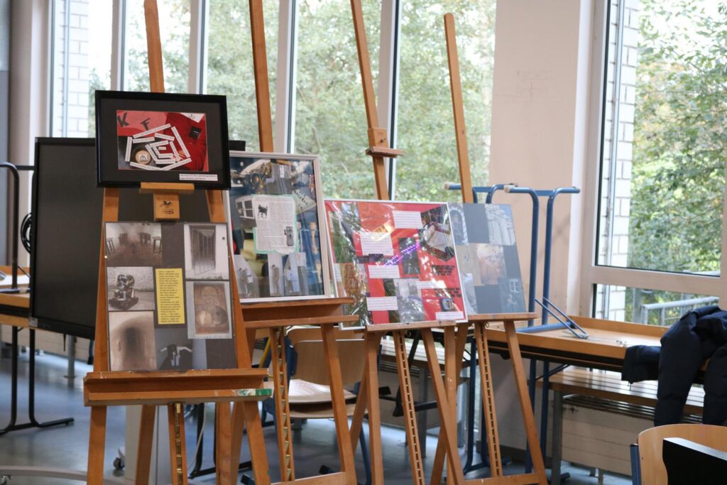 Kunstausstellung mit Bildern auf Staffeleien in einem hellen Raum.
