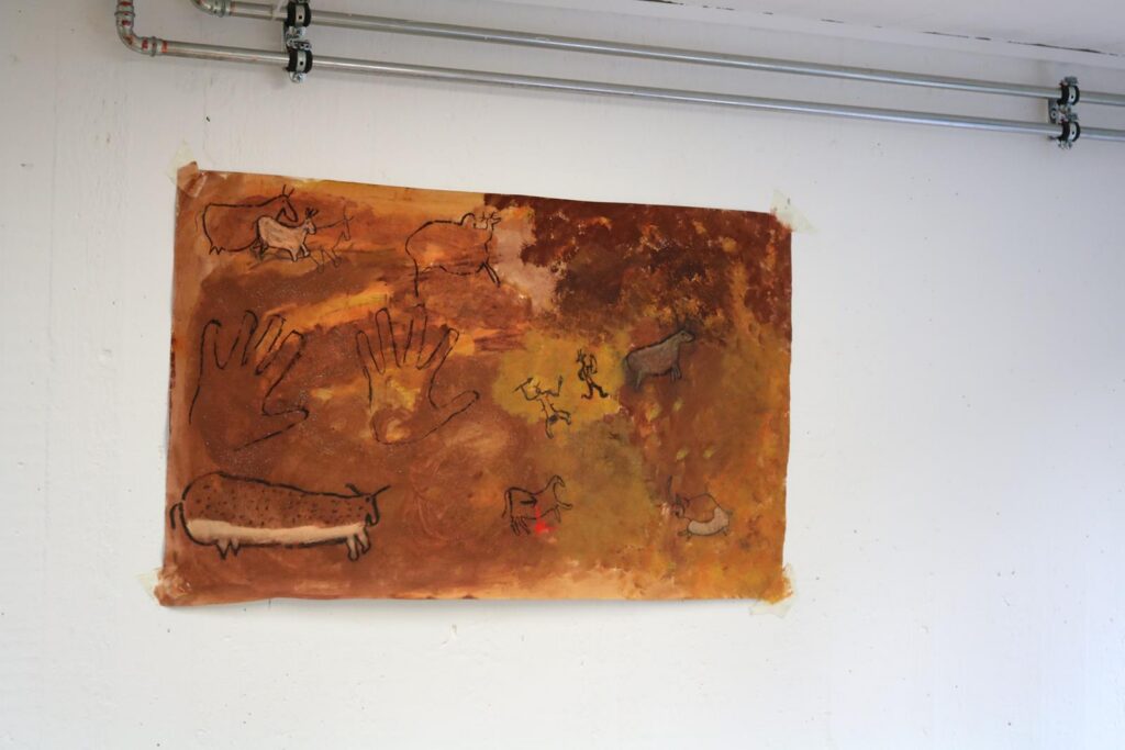 Ein Wandbild mit abstrakten, erdigen Farbtönen und verschiedenen Tier- und Handdarstellungen.