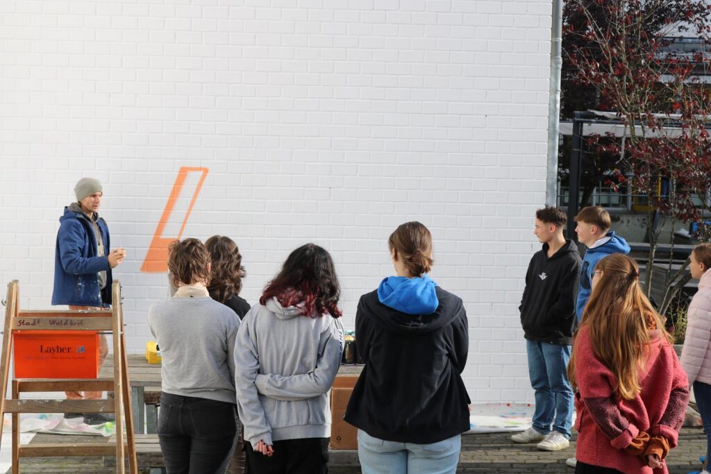 Gruppe von Schülern hört einem Lehrer an einer Wand zu.
