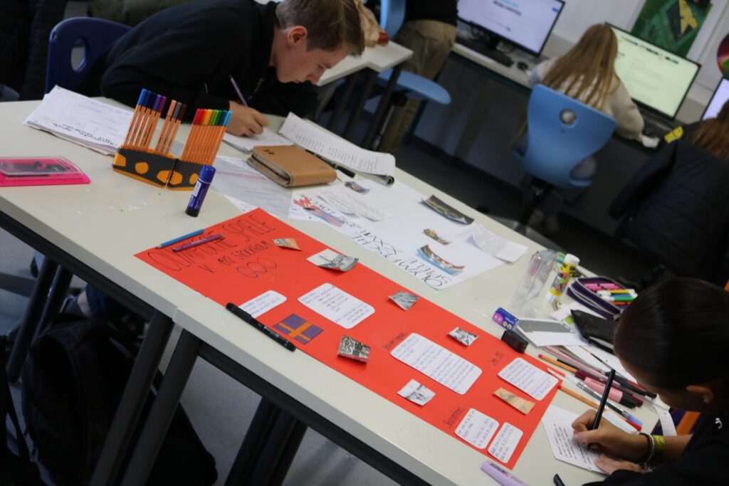 Schüler arbeiten an Projekten an einem Tisch mit Materialien und Computern.