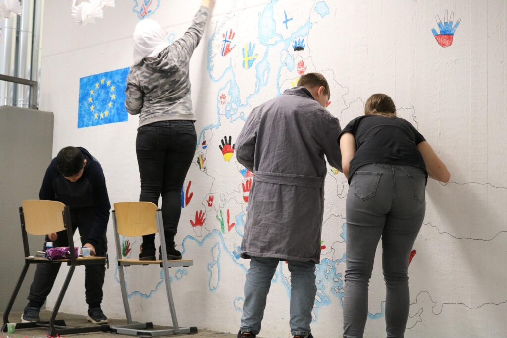Schülerinnen und Schüler malen ein Wandbild mit bunten Handabdrücken.