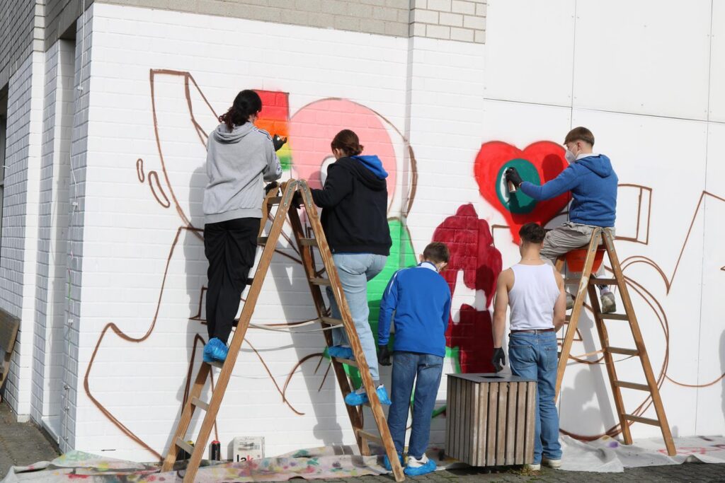Schülerinnen und Schüler gestalten gemeinsam eine Wand mit Graffiti.