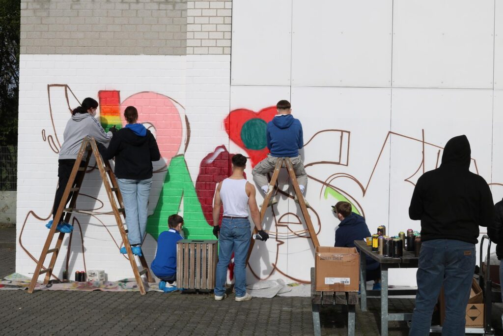 Schüler arbeiten an einem großen Wandgemälde in bunten Farben.