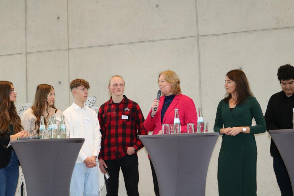 Gruppendiskussion mit mehreren Personen an Stehtischen, eine Person spricht ins Mikrofon.