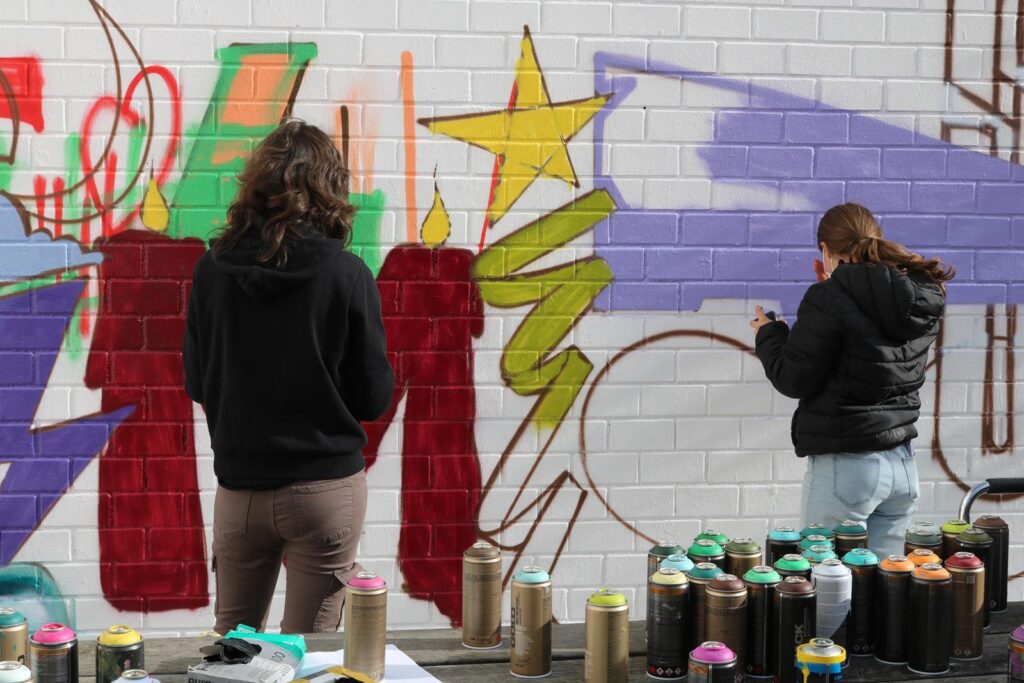 Zwei Personen sprayen an einer Wand mit bunten Graffiti.