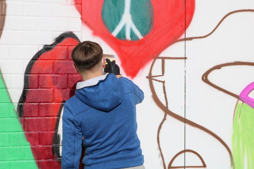 Ein junger Mensch malt an einer bunten Wand.