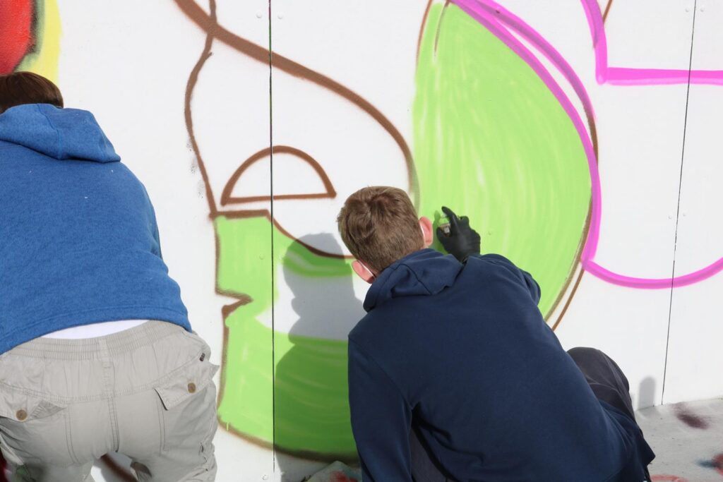 Zwei Personen sprayen farbige Grafiken auf eine Wand.