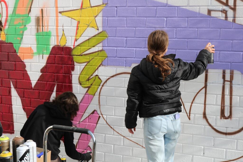 Zwei Kinder sprühen Graffiti an eine Wand.