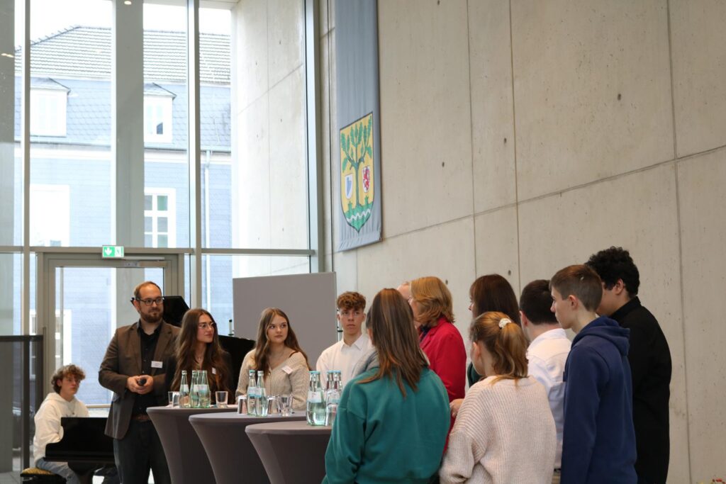 Schüler und Erwachsene stehen an Stehtischen bei einer Veranstaltung.