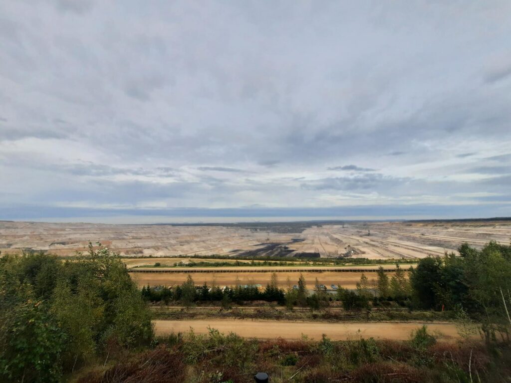 Weite Landschaft mit Abbaugebiet, freiem Himmel und angrenzendem Wald.