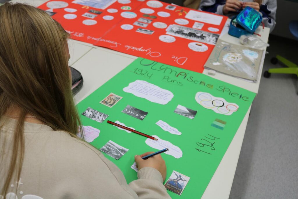 Schülerin erstellt ein Plakat mit Bildern und Texten auf grünem Papier.
