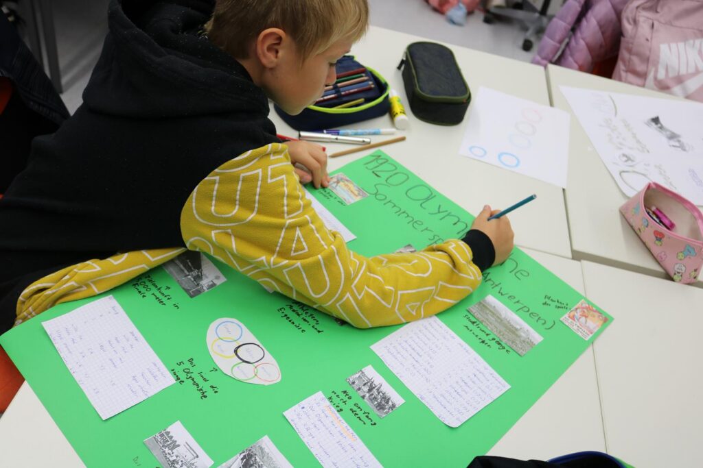 Schüler arbeitet an einem grünen Plakat mit Texten und Zeichnungen.